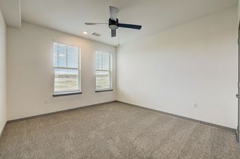 An empty living room with a ceiling fan and two windows